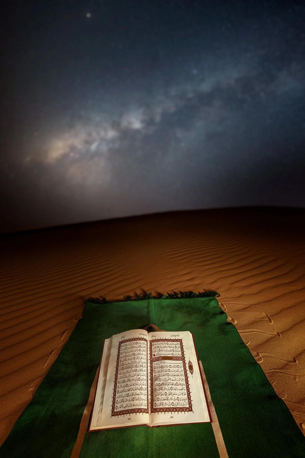 Open Holy Quran on a green prayer rug laid out on desert sand ripples under starlit sky in Qatar by Hammad Iqbal