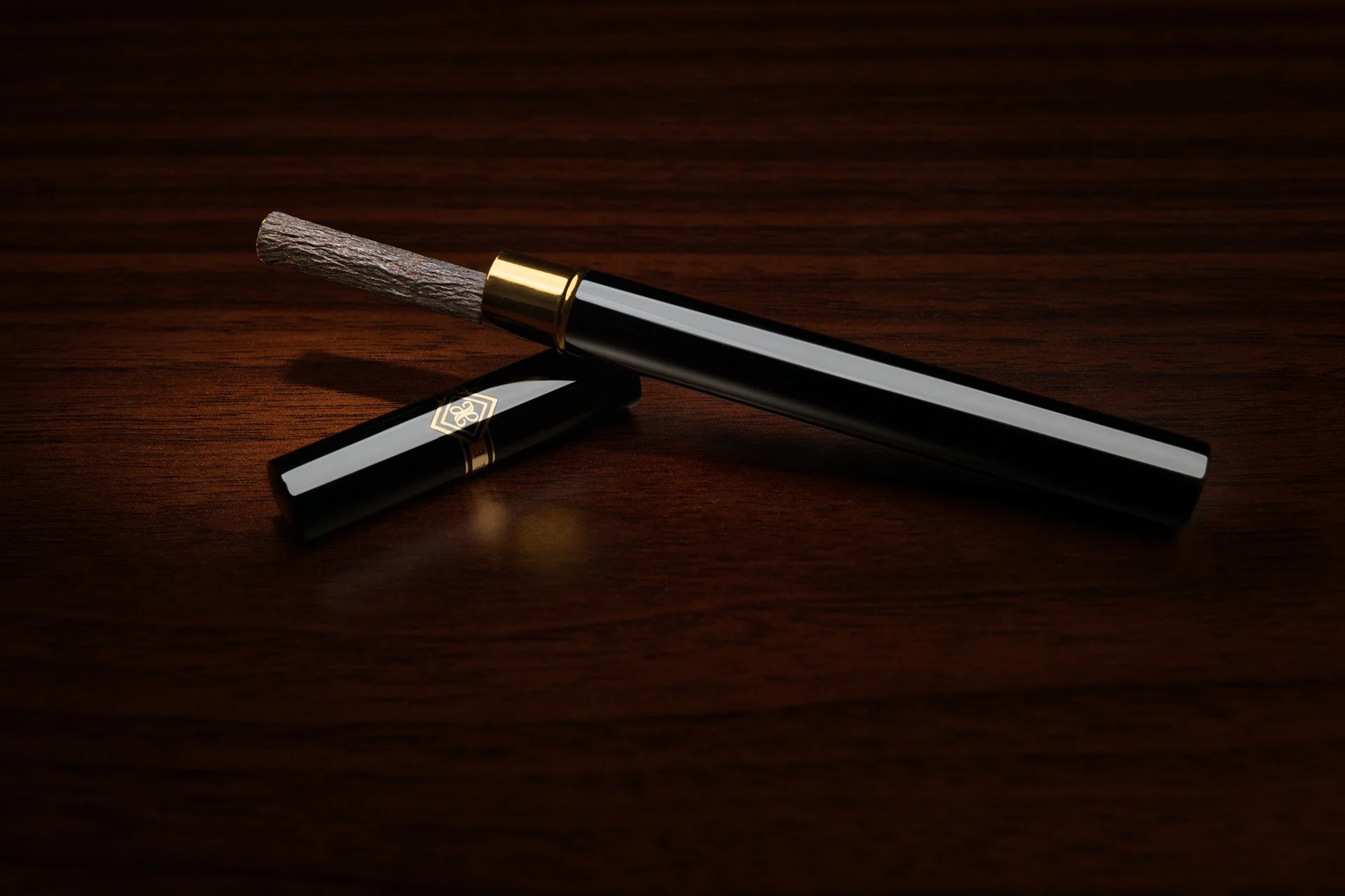 Product studio shot of uncapped black case showing natural miswak bristles resting on mahogany table by Hammad Iqbal