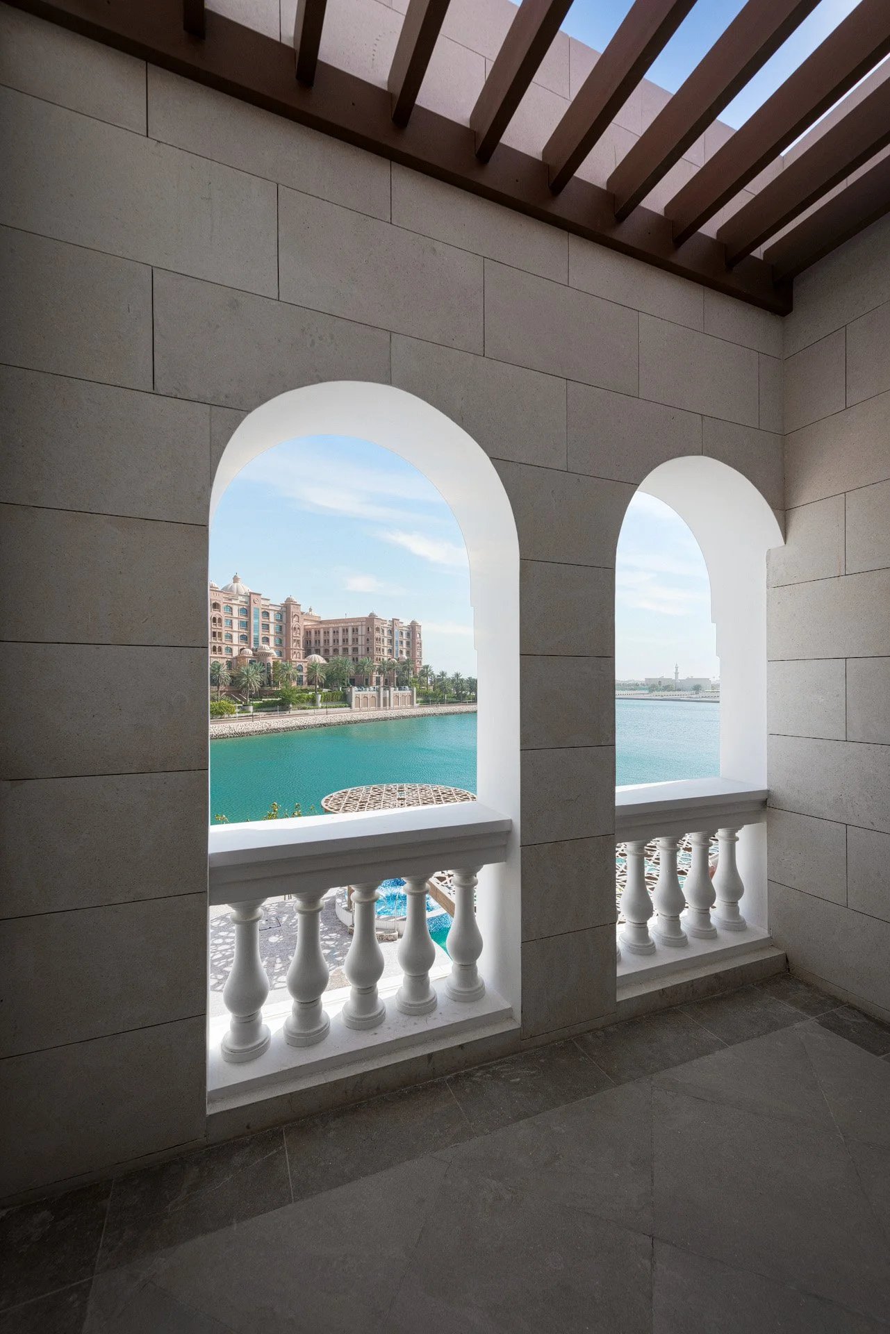 View through a classical white arched balcony looking across the blue lagoon toward Marsa Malaz Kempinski at a luxury villa in The Pearl Qatar by Hammad Iqbal