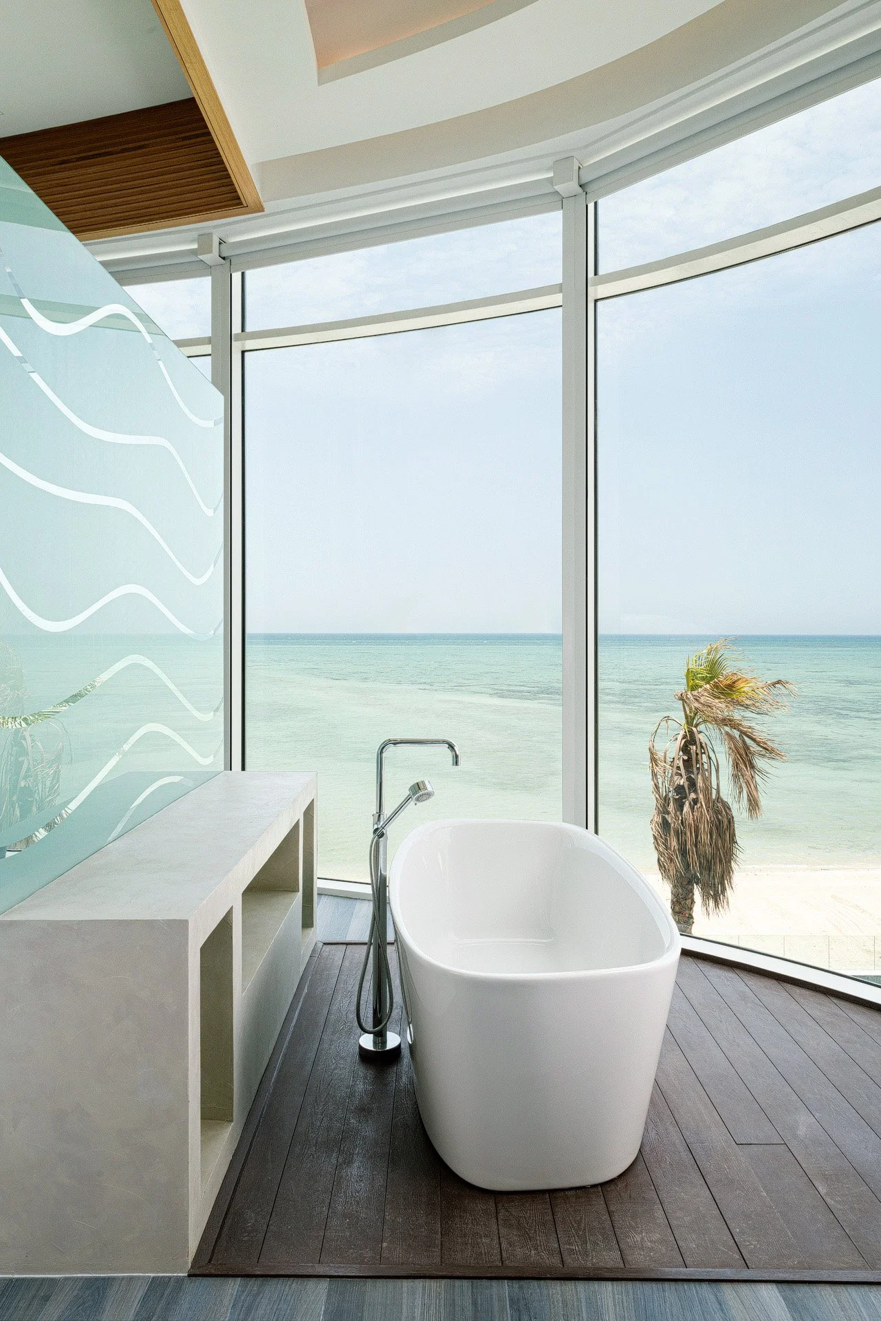 Freestanding soaking bathtub positioned in front of panoramic ocean view floor to ceiling windows in a Qatar villa by Hammad Iqbal
