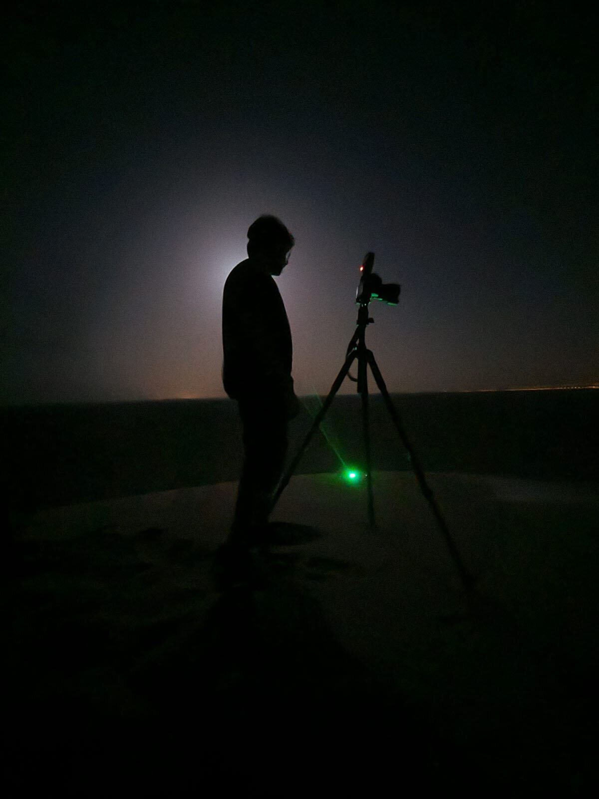 Behind the scenes photo of photographer Hammad Iqbal using a laser pointer to acquire focus in total dark desert night