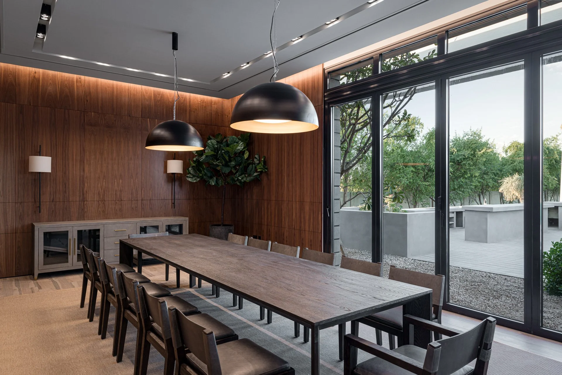 Long timber dining table surrounded by leather chairs and black dome pendant lights in a luxury Qatar pavilion by Hammad Iqbal