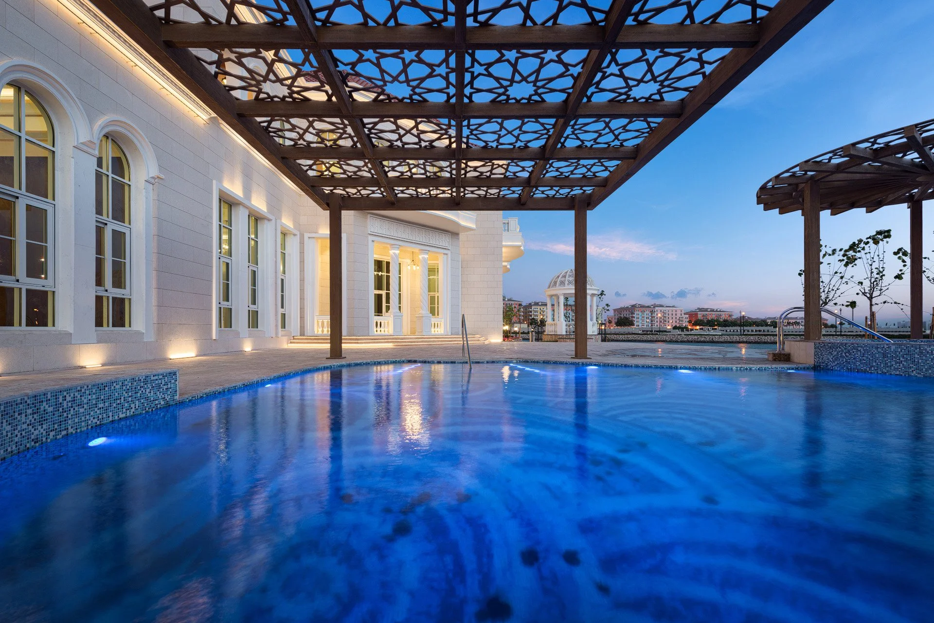 Twilight photo across glowing infinity pool looking at classical white arched villa windows in The Pearl Qatar by Hammad Iqbal