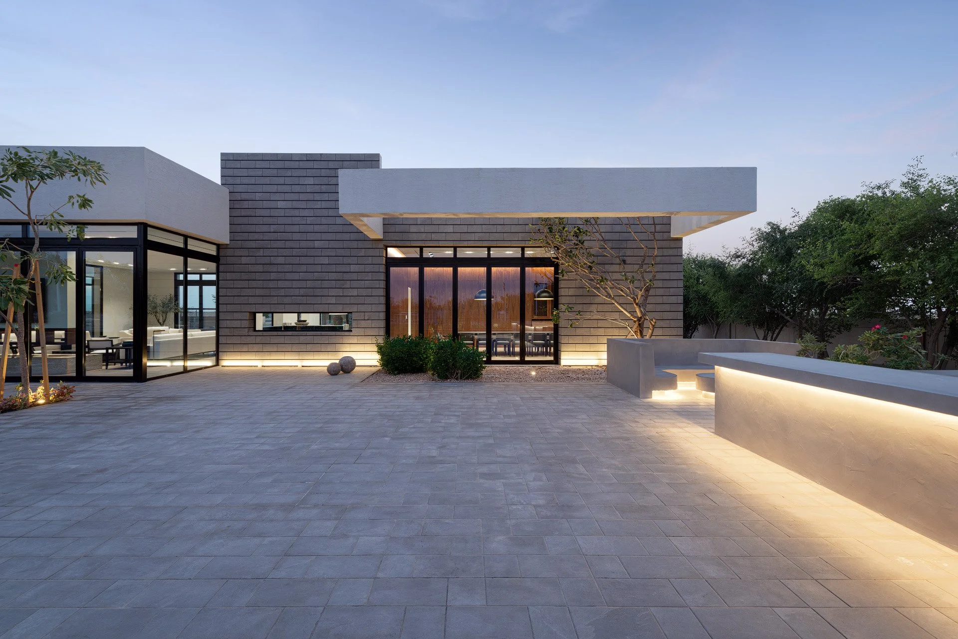 Modernist stone facade and paved patio with integrated warm architectural lighting at a private Qatar estate by Hammad Iqbal