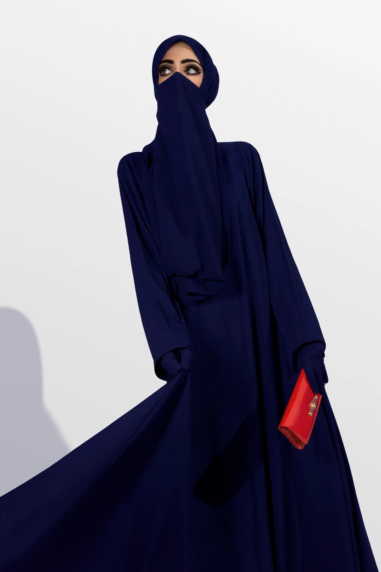 Full length fashion shot of flowing navy abaya accessorized with a vibrant red clutch bag by Hammad Iqbal