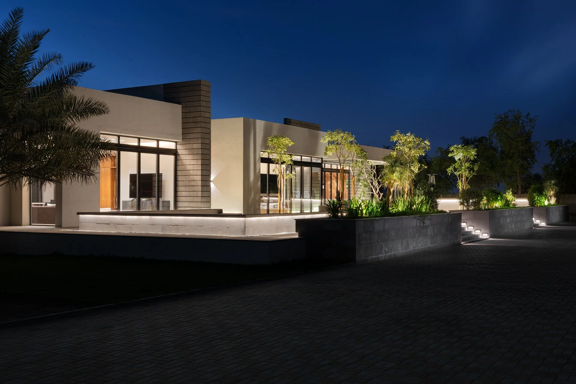 Twilight exterior photo of modern entertainment pavilion with illuminated raised planters and deep blue sky by Hammad Iqbal