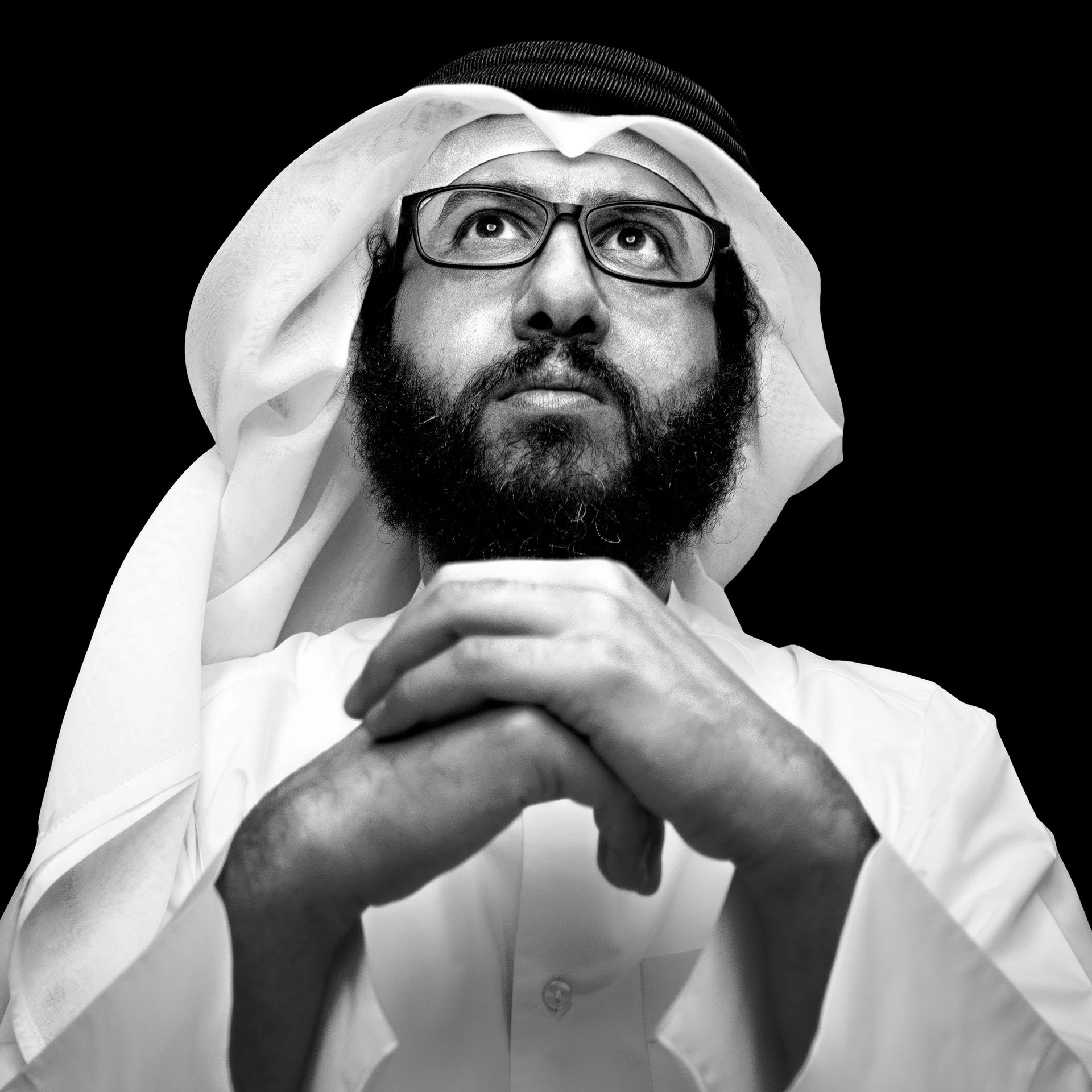 Dramatic black and white wide angle portrait of attorney Abdulla Mohammed Al-Mulla looking upward with hands clasped by Hammad Iqbal
