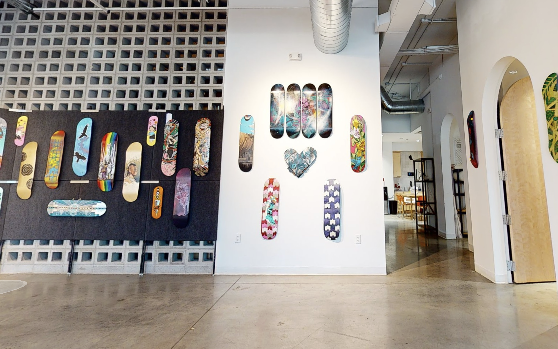 Indoor art gallery displaying skateboard decks with various colorful designs and patterns on a black and white wall.