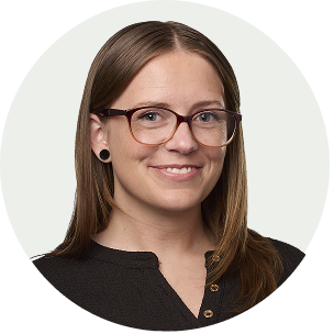 A woman with long brown hair, glasses, and black earrings smiling at the camera, wearing a black top with a buttoned collar.