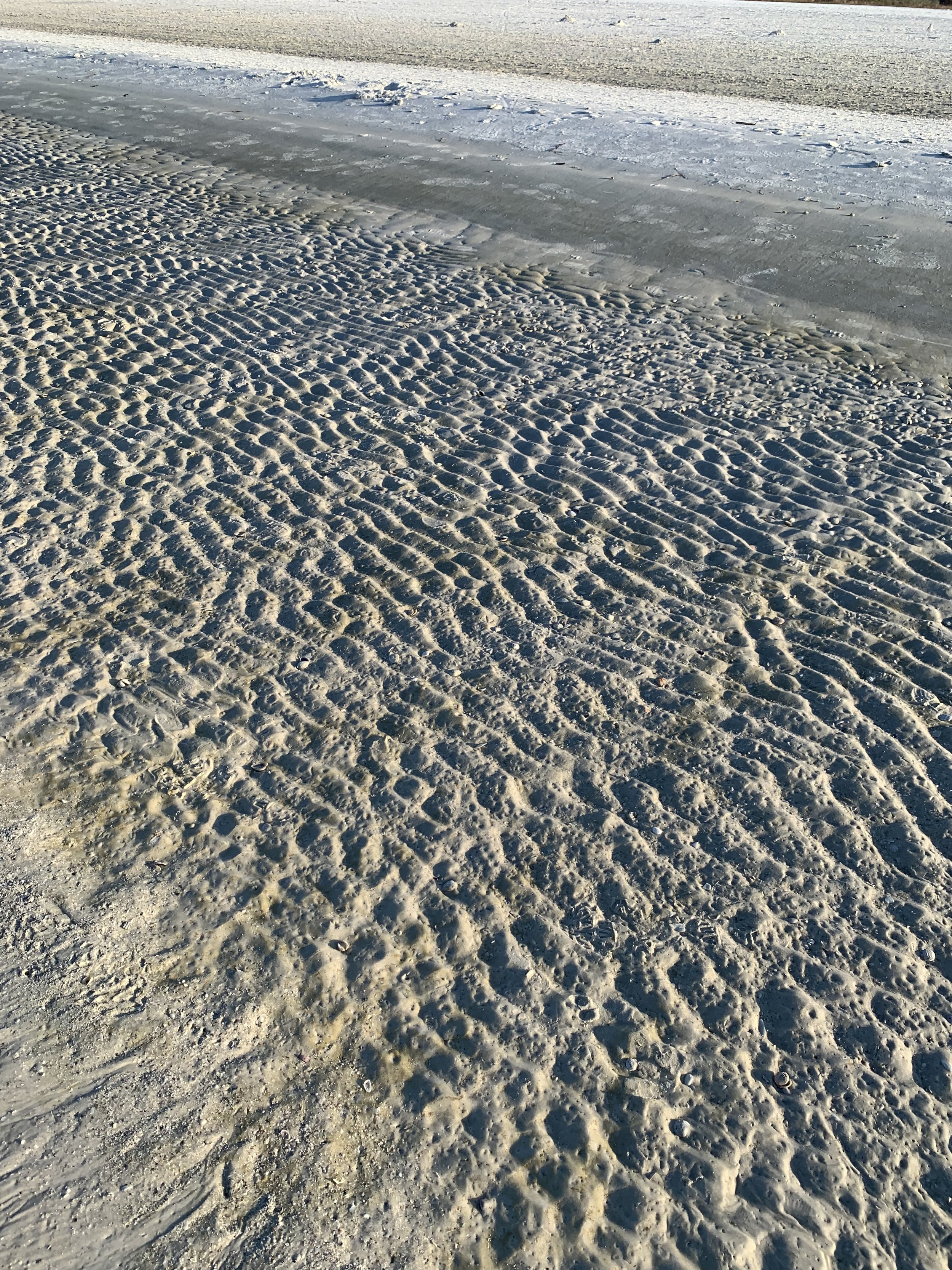 Sand textures on a beach with patterns formed with the waves and wind, along  with calm water and shoreline