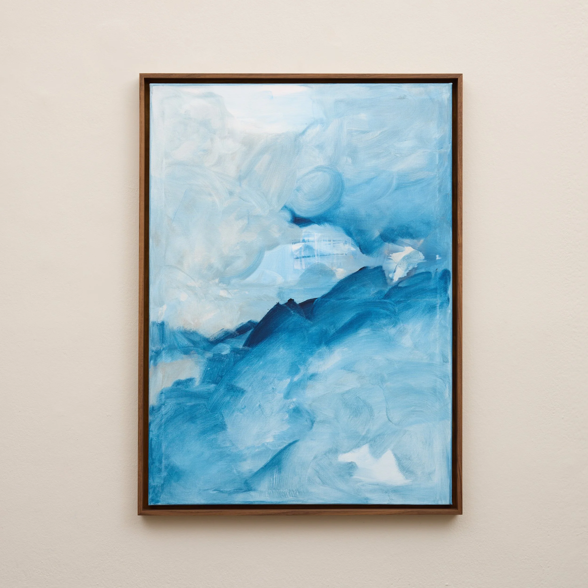A framed abstract painting with shades of blue, white, and black on a neutral wall.