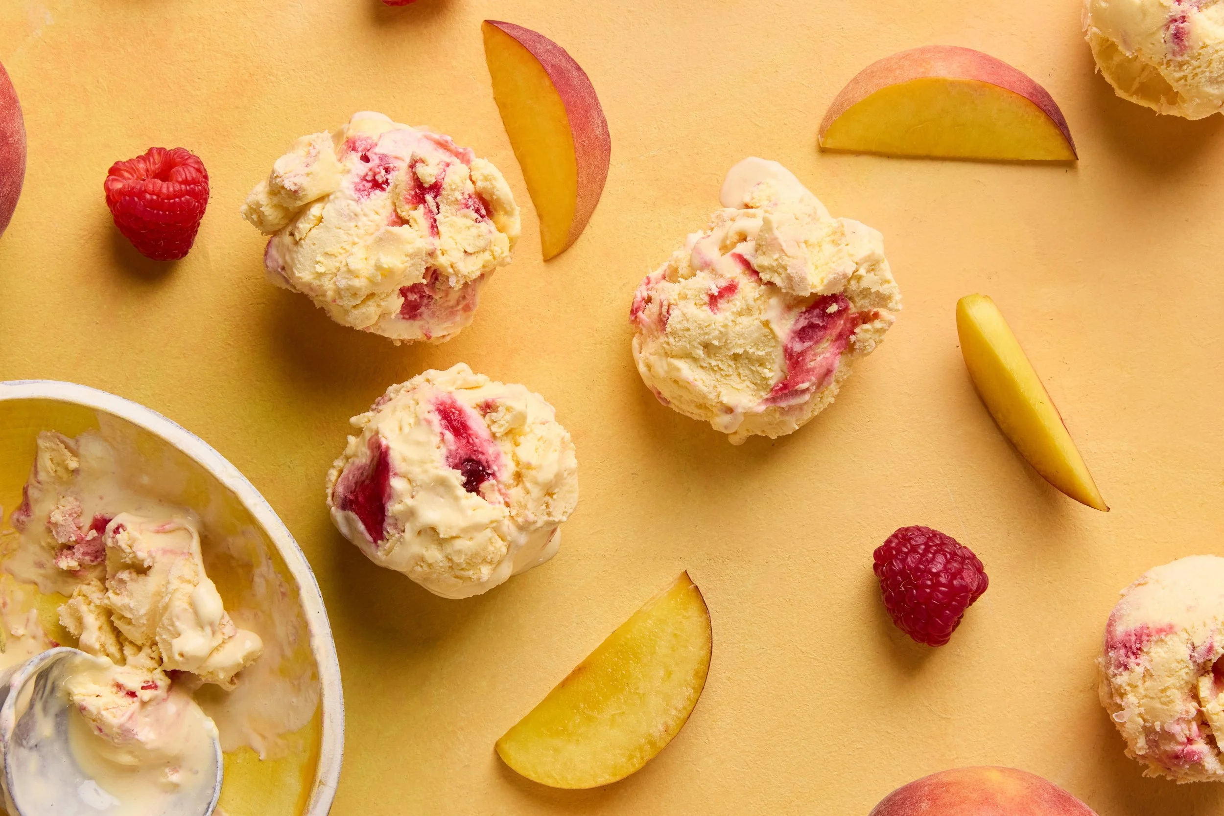 Two ice cream cones with vanilla ice cream, dipped in chocolate and chopped nuts, placed in a glass on a white wooden surface. An additional scoop of ice cream and an ice cream scoop are nearby.
