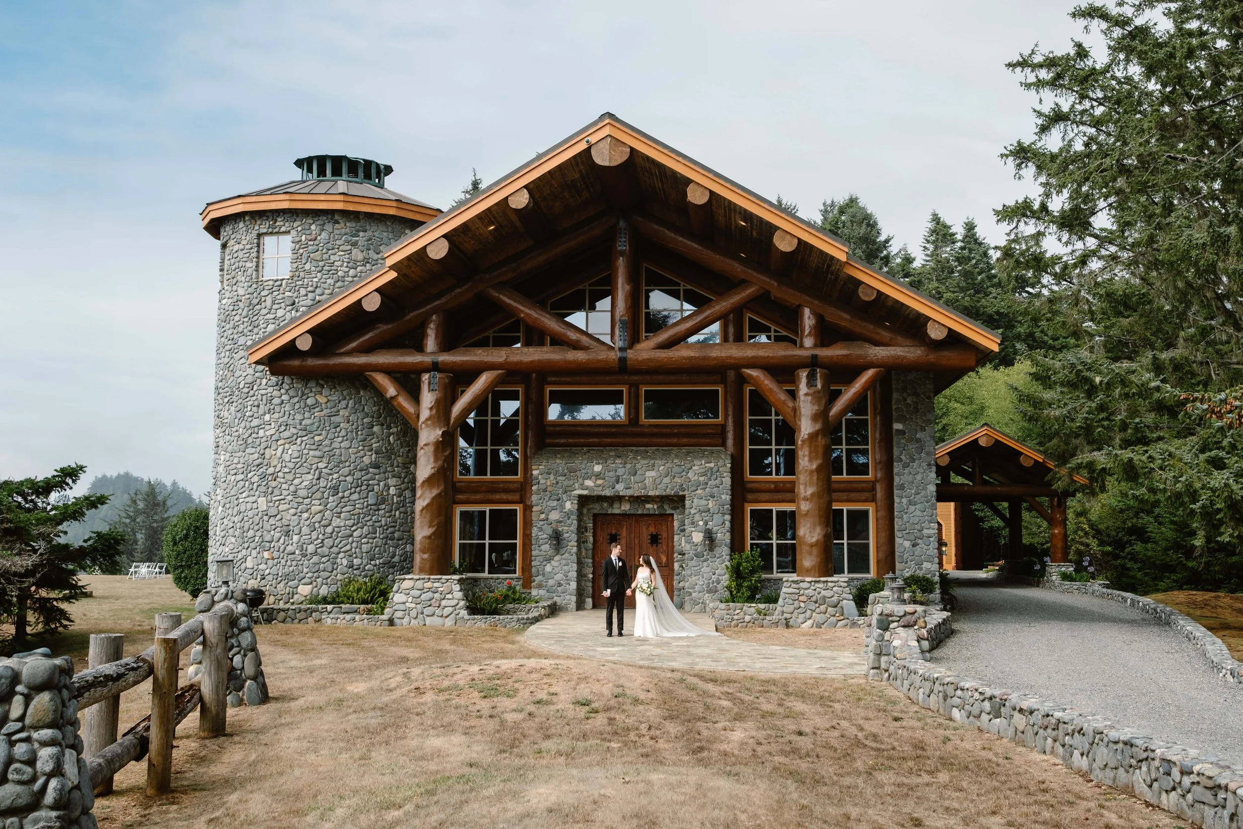 Bride and groom standing in front of a large coastal stone and timber lodge wedding venue.