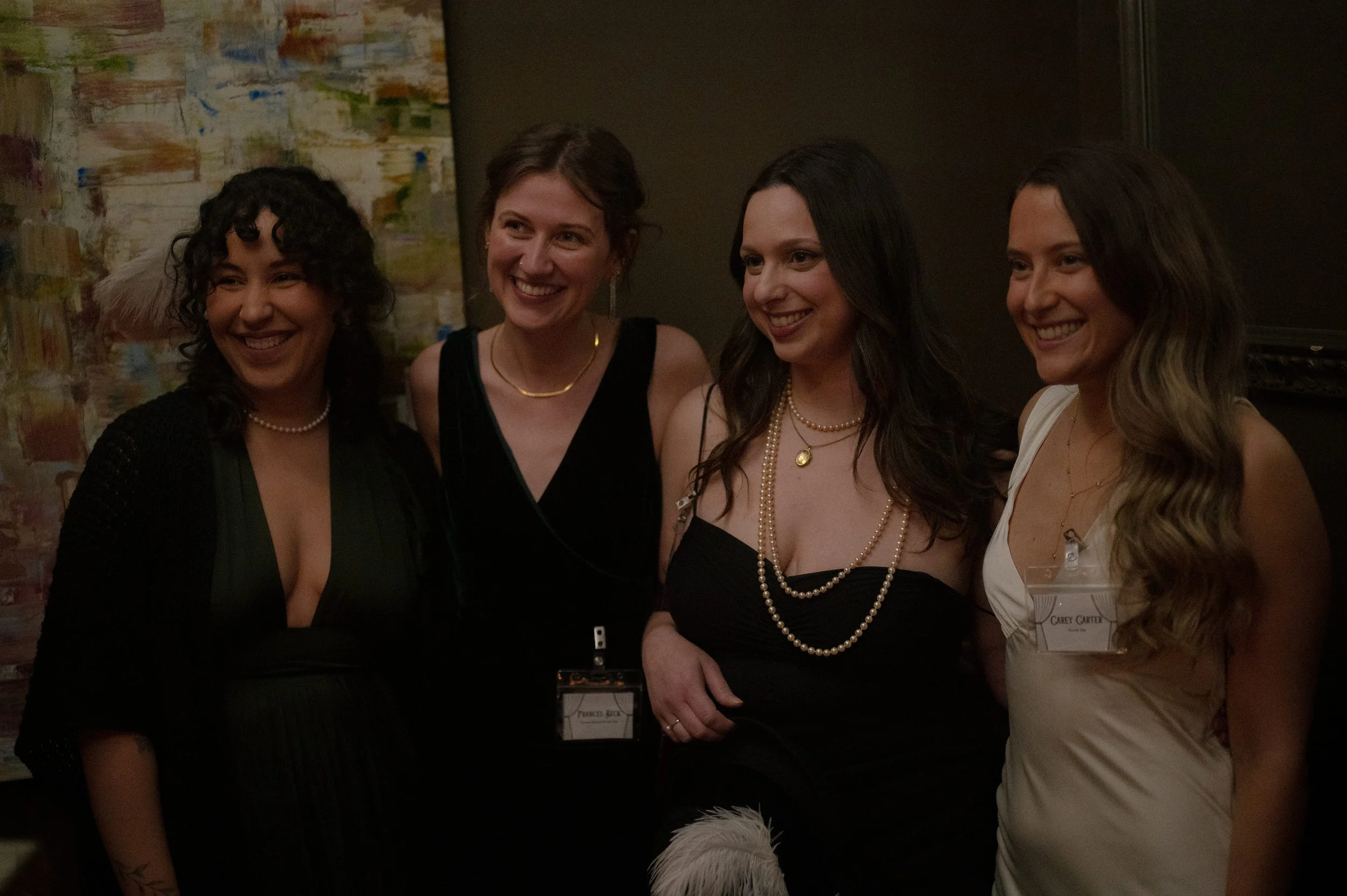 Guests in 1950s Hollywood outfits with pearl necklaces smiling together at a murder mystery party, vintage glam costumes for Behind the Curtain game night