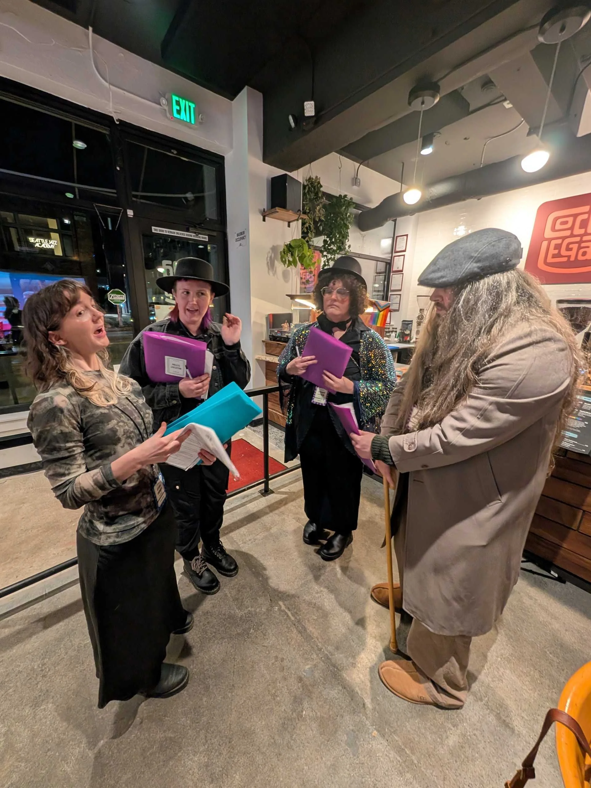 Four murder mystery players stand in a circle holding character packets and debating clues as part of the investigation.