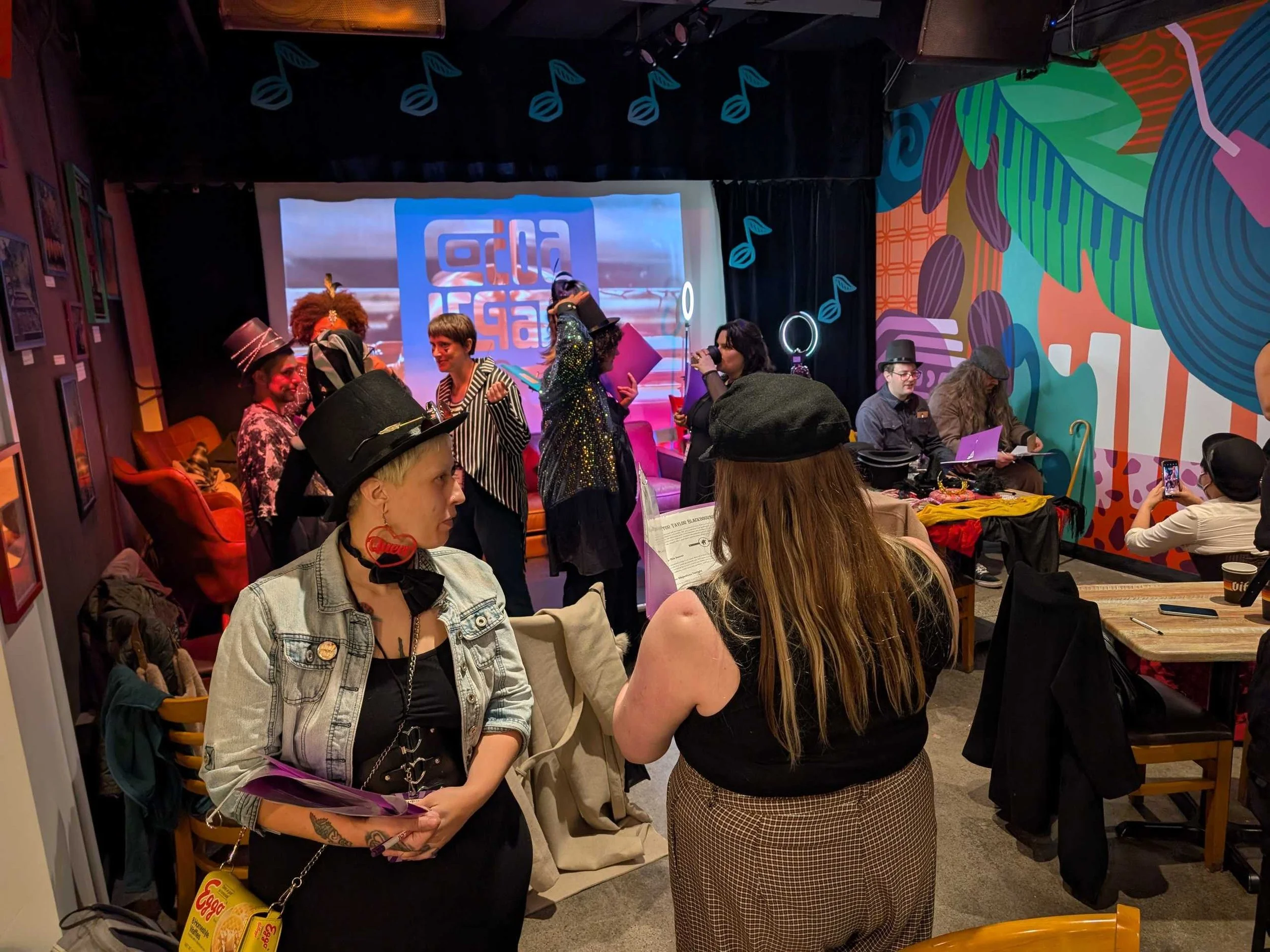 Two murder mystery players in striped and vintage-inspired outfits talk closely while holding character folders during gameplay.