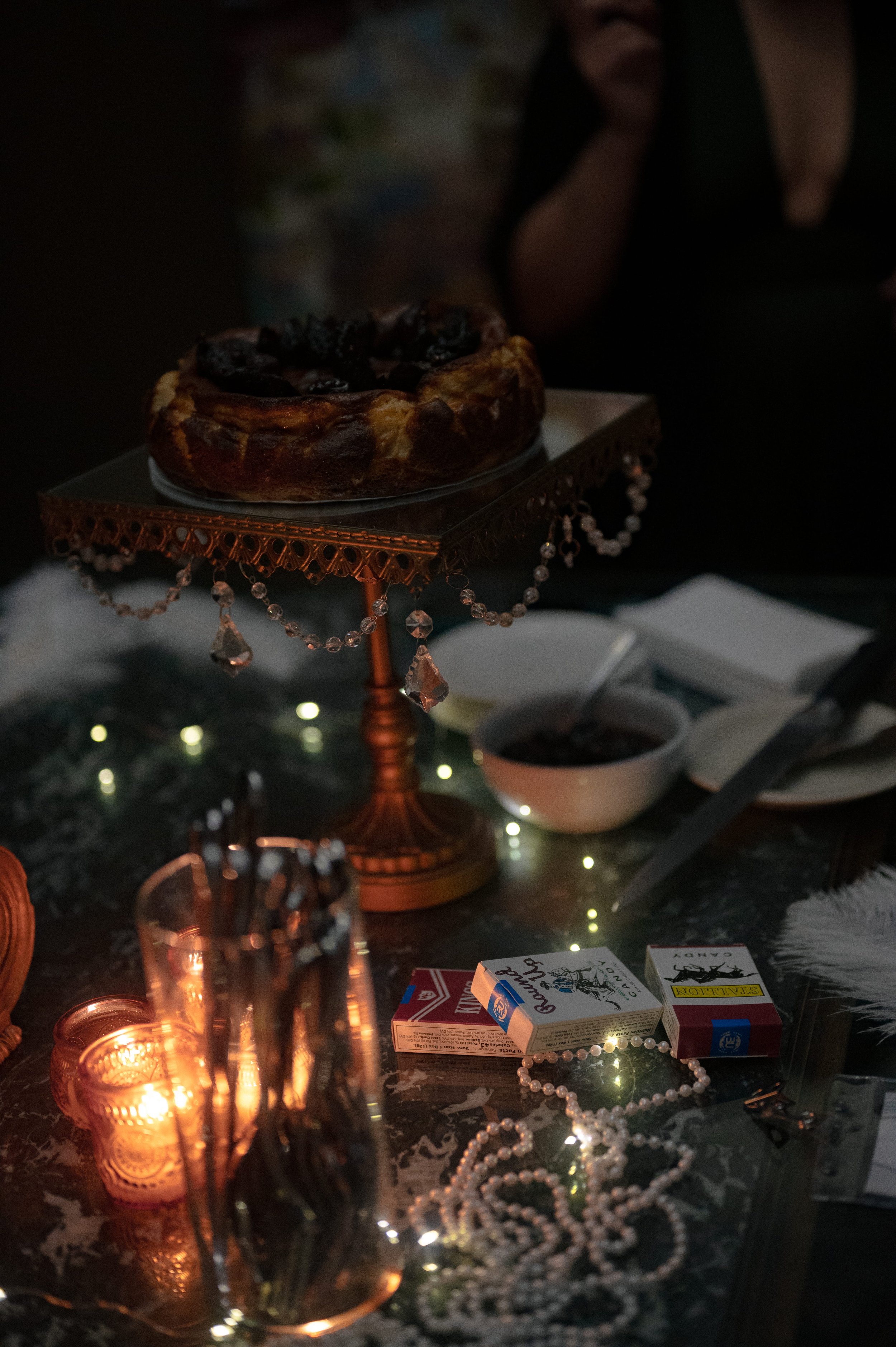 Vintage Hollywood party dessert table with cake on gold stand, candles, pearls, and playing cards, styled for a 1950s murder mystery party theme Behind the Curtain