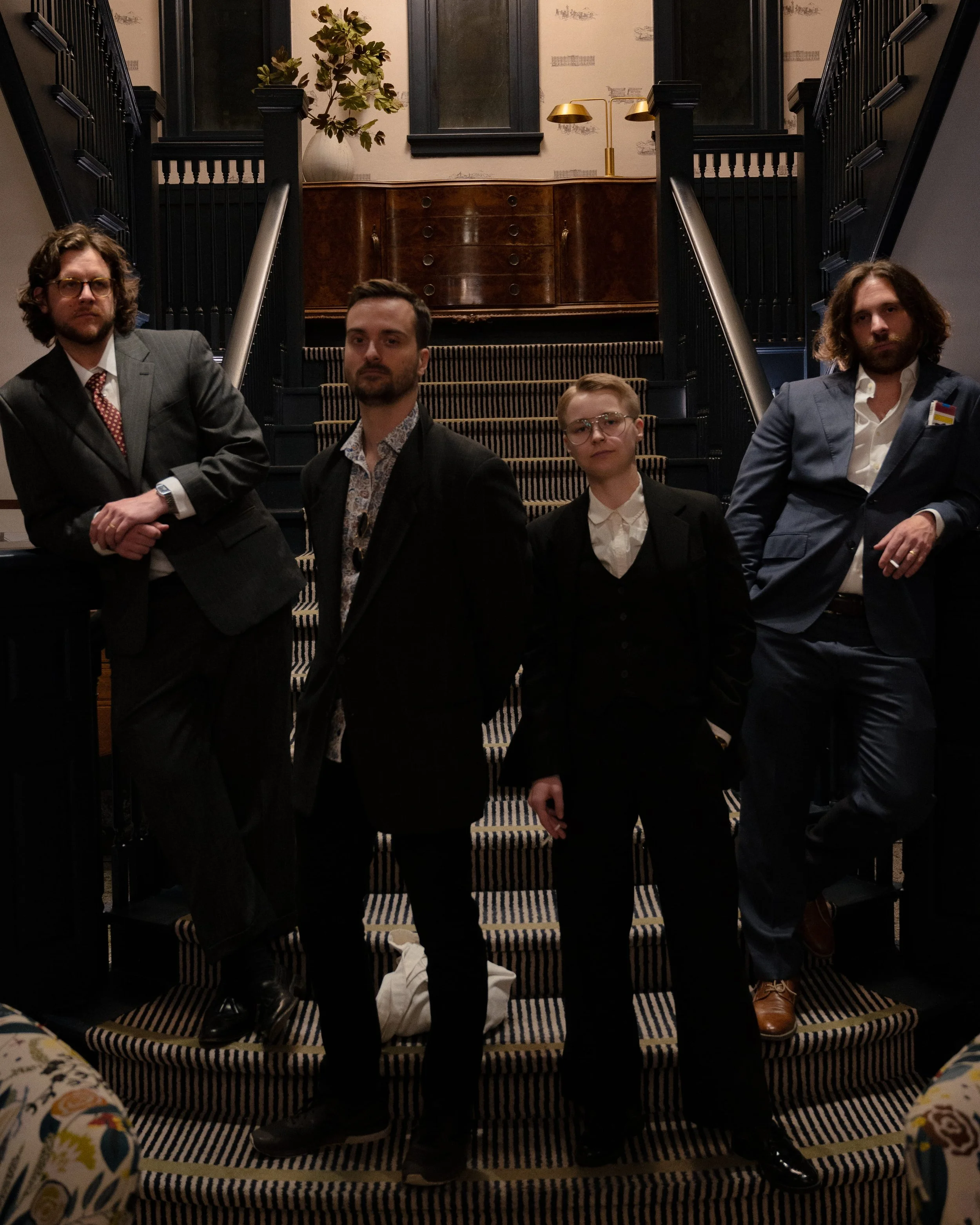 Guests in suits posing on staircase in 1950s Hollywood style outfits, cinematic murder mystery party scene for Behind the Curtain game
