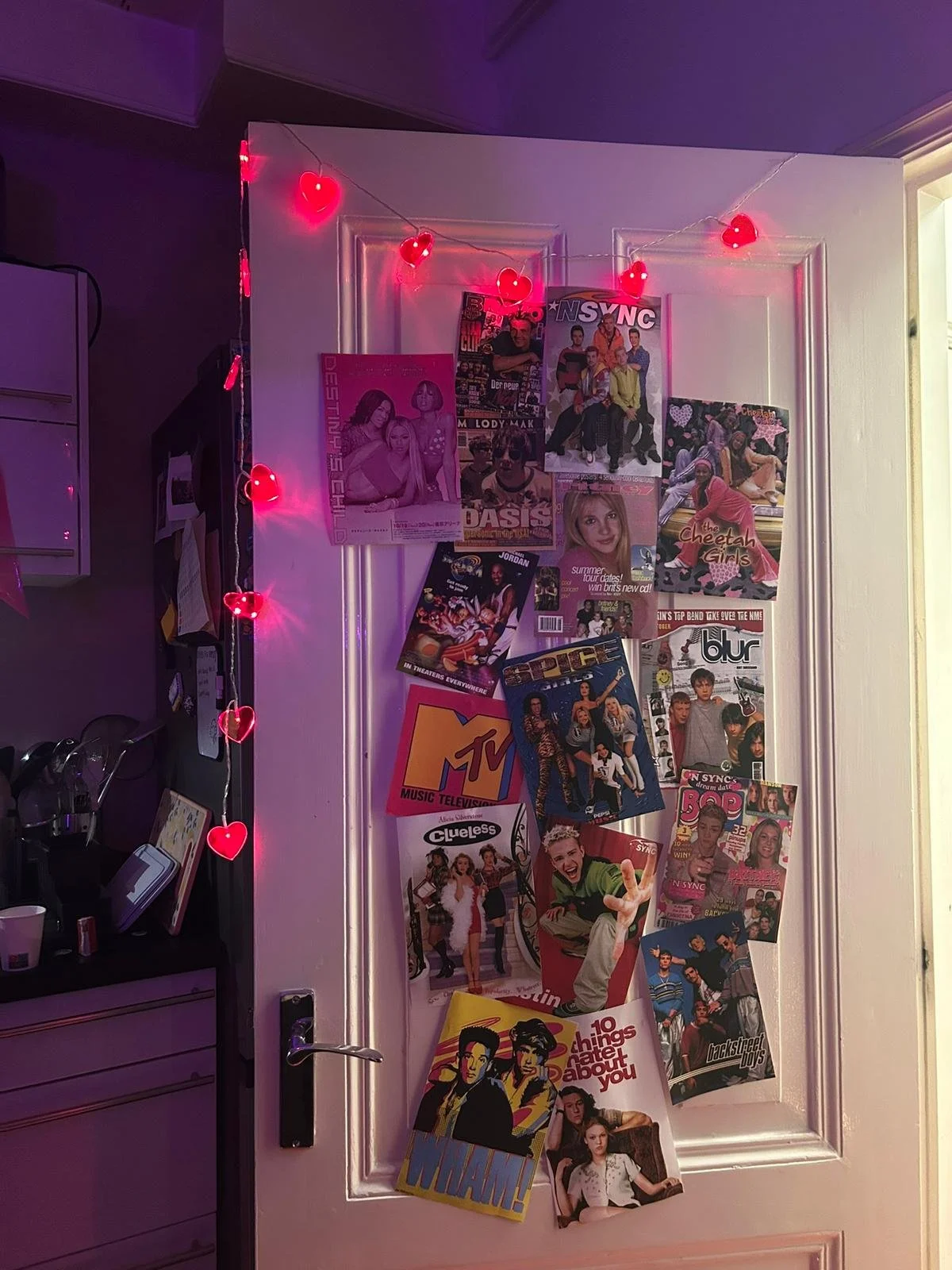 90s themed party decor with bedroom door covered in *NSYNC, Spice Girls, MTV, and teen magazine posters with heart string lights for nostalgic murder mystery party atmosphere