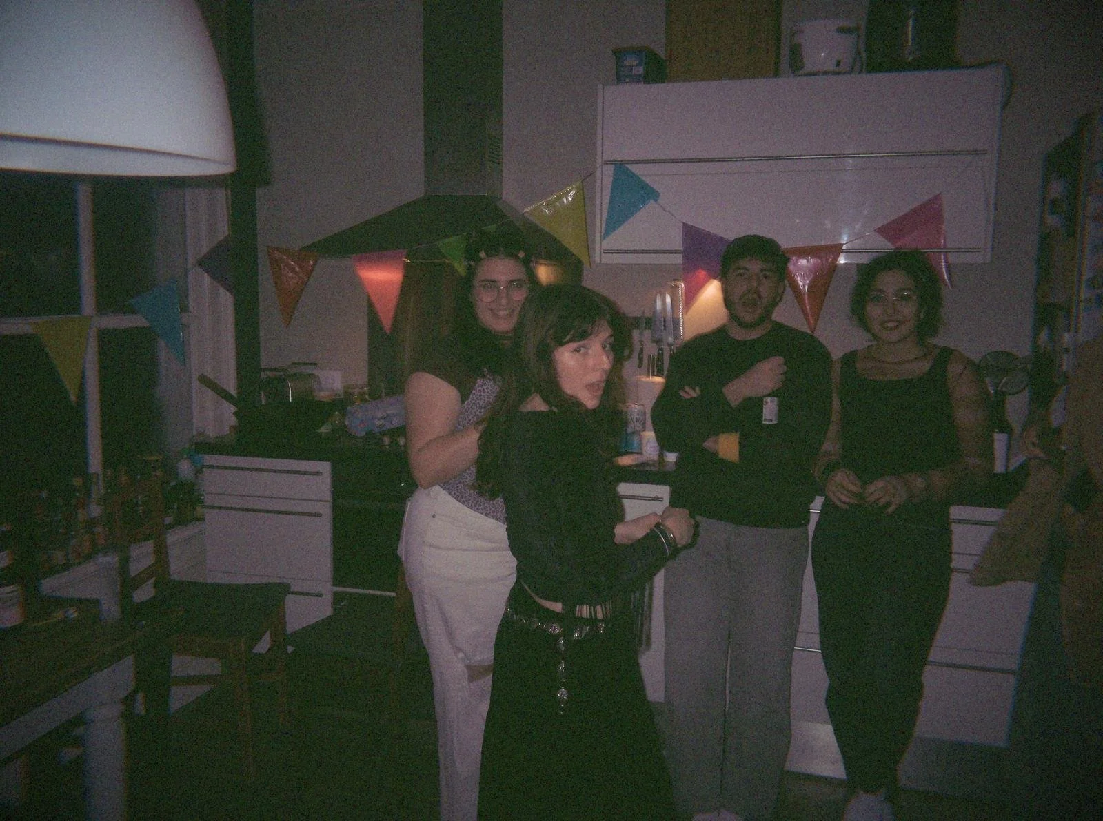 Guests in 90s outfits playing a murder mystery party game in a decorated kitchen with bunting and party decorations for interactive themed party experience