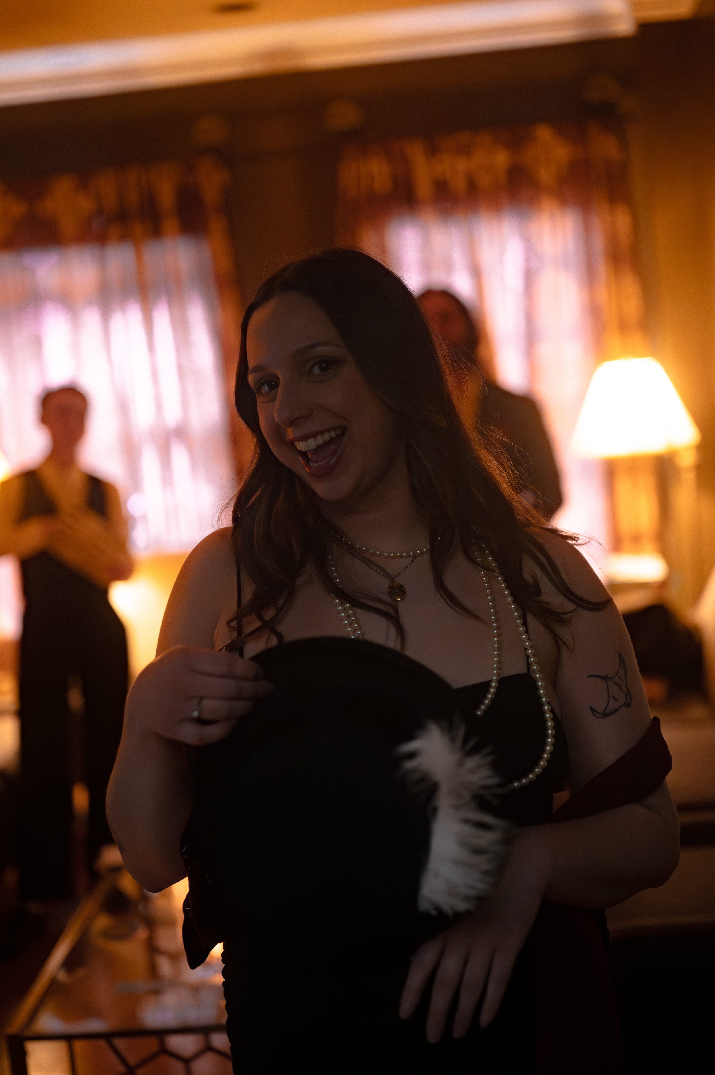 Guest in black dress with pearls and feather accessory posing at a 1950s Hollywood murder mystery party, glamorous vintage costume for Behind the Curtain game