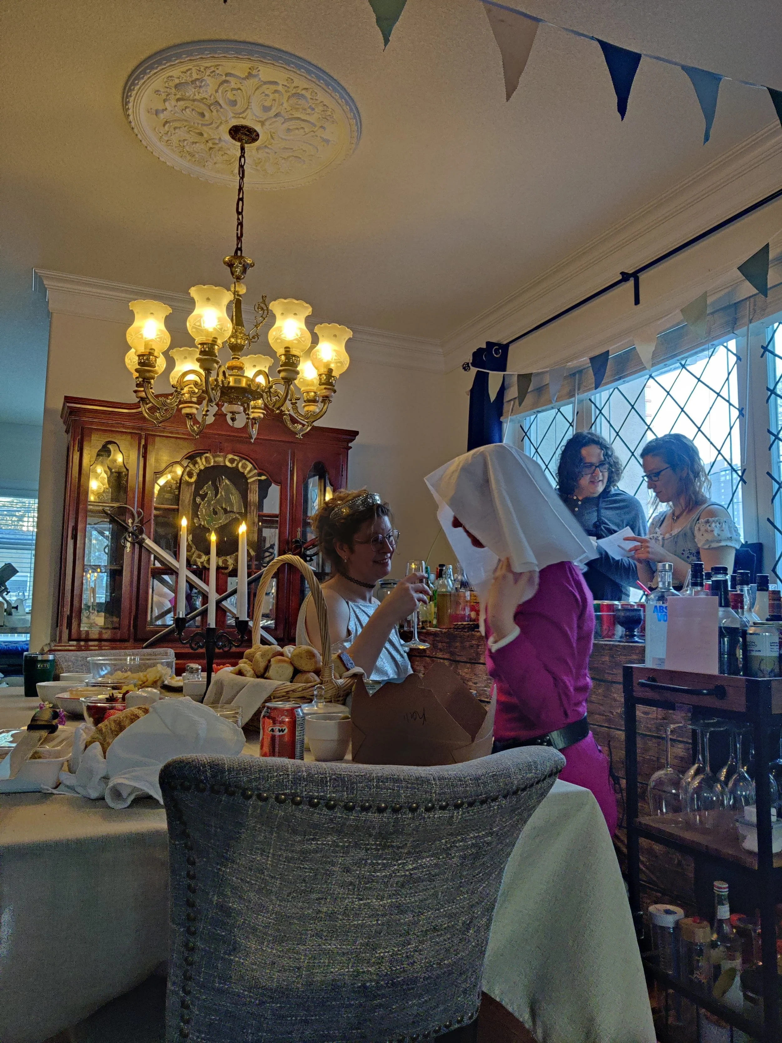 Guests in fantasy costumes gathered at a murder mystery party table with drinks and props, playing an interactive roleplaying game