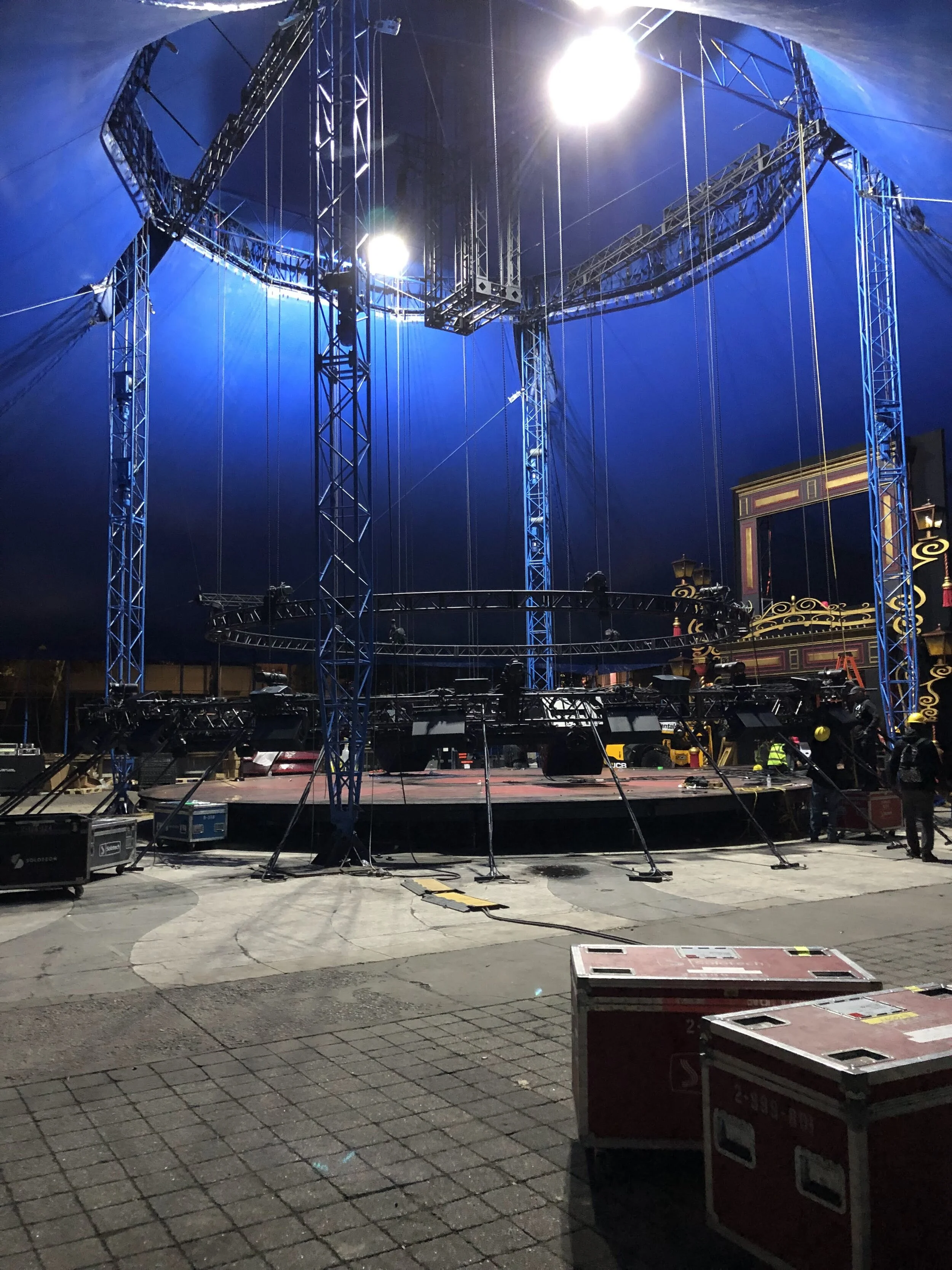 Stage setup with blue lighting and metal truss structure inside a circus tent at night.