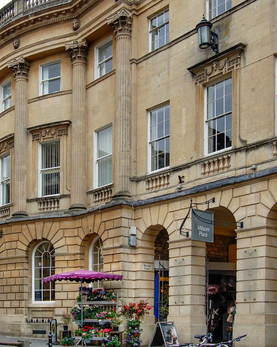 ~
.
.
The Little Flower Stand
.
.
This image caught my eye because of how the diminutive little flower stand, with its purple shade umbrella, was simply dwarfed by the impressive architecture of this beautiful building in Bath, England. The umbrella 