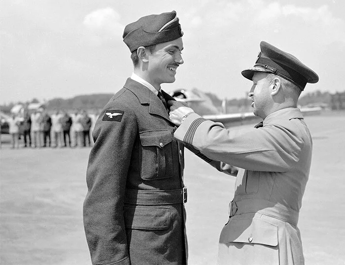 16 June 1941—Leading Aircraftman John Gillespie Magee, still wearing the white cap flash of an airman in training, beams with pride and delight as he is pinned with his RCAF wings by Group Captain Wilfred A. Curtis, DSC and Bar at No. 2 Service Flyi…