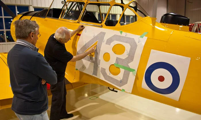 Mike Potter and Dave O’Malley work on a bare yellow canvas to apply the Second World War markings to the High Flight Harvard in 2009. Photo: Peter Handley