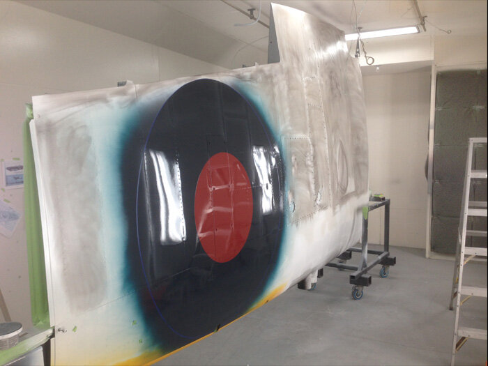   The top side of the starboard wing is being sanded to create a rough bonding surface, before final white coat will “trap” the roundel’s blue as well as the yellow leading edge. Photo: Korrey Foisy  