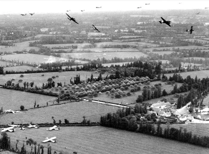 DC-3 aircraft release their Horsa gliders over the Dutch countryside. Considering the altitude we see here, the gliders likely made just one turn into the wind before turning final and landing—a wise tactic to get the helpless gliders on the ground as fast as possible. The gliders at the bottom left are all grouped together at the end of a field, indicating they landed from right to left on that stretch of open farmland. Photo: RAF