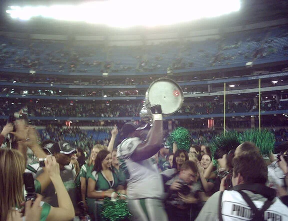 A Roughrider lineman lifts the Zapper, supported by the Grey Cup, to the zapper gods. Photo by Lauren Roberts on Flickr.com