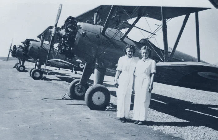 A couple of women staff at No. 32 EFTS Bowden pose on the flight line with a line-up of immaculate Boeing  PT-27 Stearmen “Kaydet” aircraft. When the 300 PT-27 trainers were returned to the USA over a period of many months, some of them, like FJ875 were re-engined and rebuilt to the PT-17 Standard of the USAAC. Photo via Clarence Simonsen