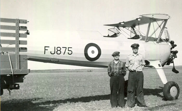 After its accident at Netook, and with its wings and empennage removed, the Stearman’s tail was lifted and tied to the bed of a farm truck and towed back the few miles to Bowden. Here we see FJ875 with what appear to be locals (the man in the military style cap is not an officer in the RAF or RCAF—possibly the truck driver). Photo via Clarence Simonsen