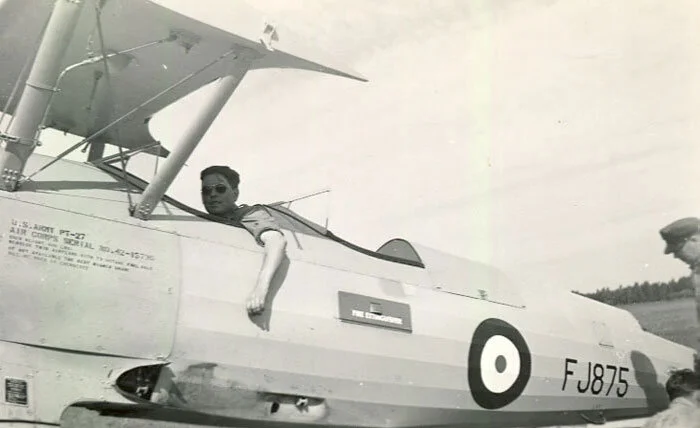 Boeing Stearman FJ875, which is today the Warrant Officer Harry Hannah Stearman, is seen at Netook in 1943, shortly after it collided on the ground with another Stearman while taxiing on the grass. Riggers from Bowden arrived soon after and removed the wings and empennage from the damaged aircraft. While mechanics work at the tail, one, in aviator sunglasses, relaxes in the cockpit, perhaps toeing the brakes and poses for the RAF photographer sent out to take photographs of the incident’s aftermath. It was this photograph that the Stearman pilots and the Netook cadets of today would recreate when the Yellow Wings team paid a visit last week. Photo via Clarence Simonsen
