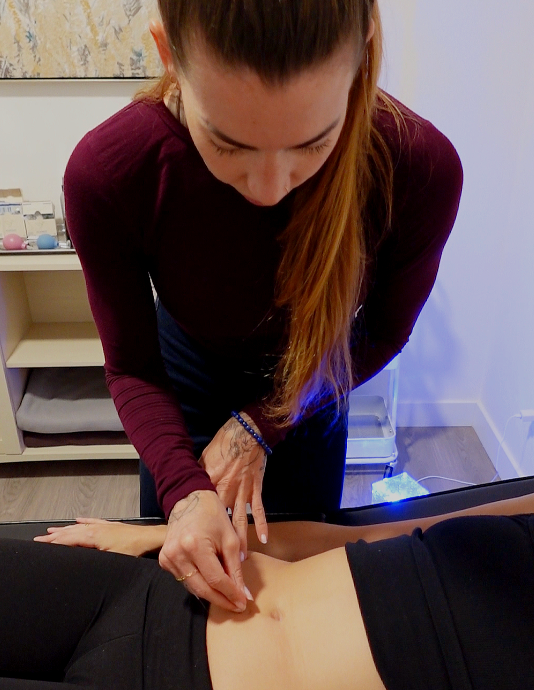 A woman with long hair performing acupuncture on a person lying face down on a treatment table.