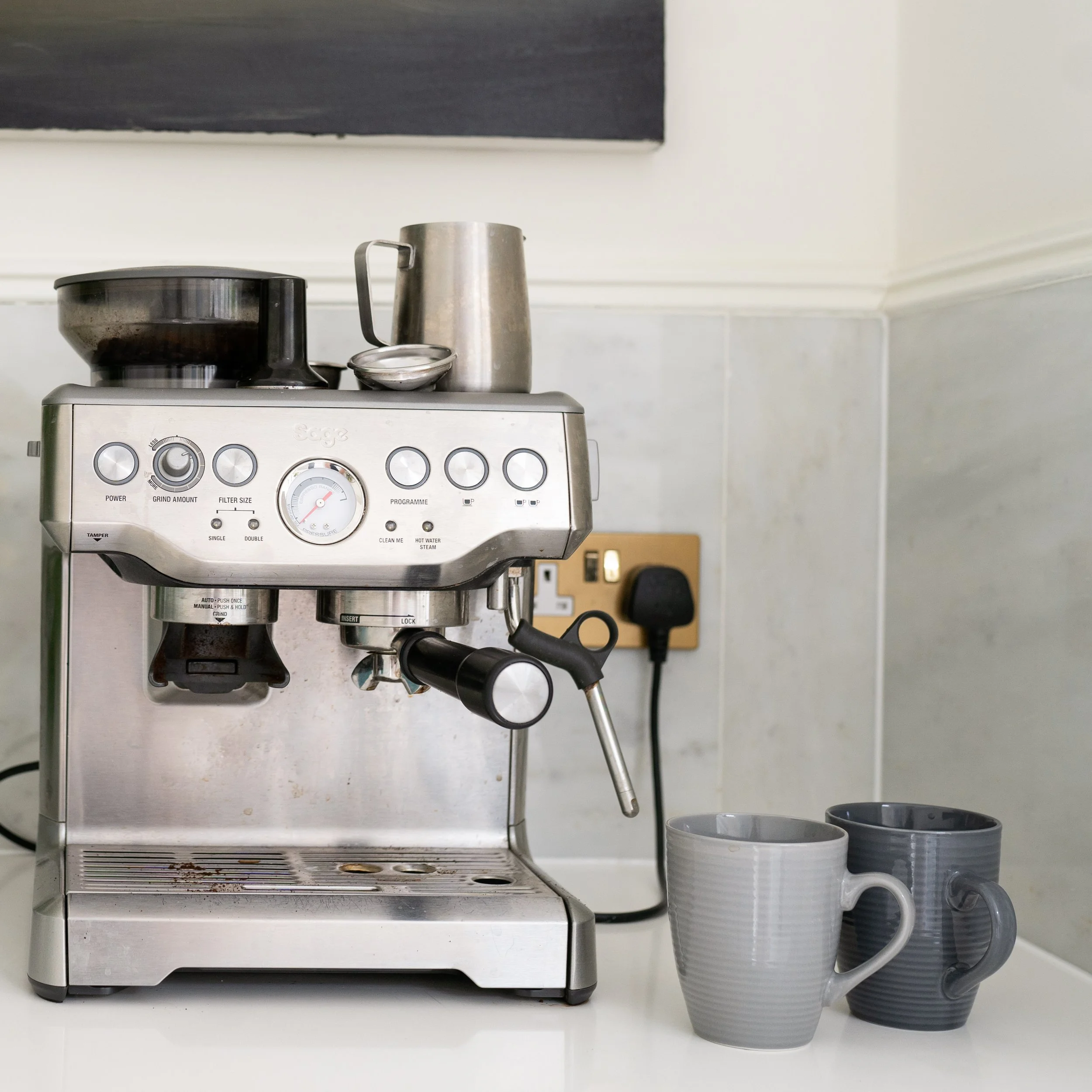Stainless steel coffee machine on a kitchen counter with two grey mugs beside it.