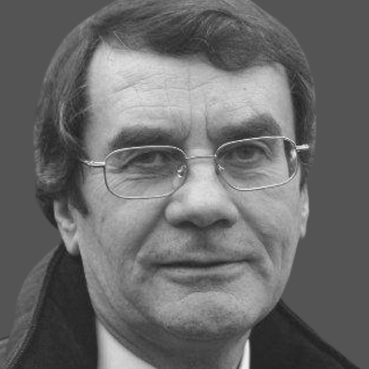 Black and white portrait of a middle-aged man with glasses, short dark hair, and a slight smile, wearing a dark coat against a plain background.