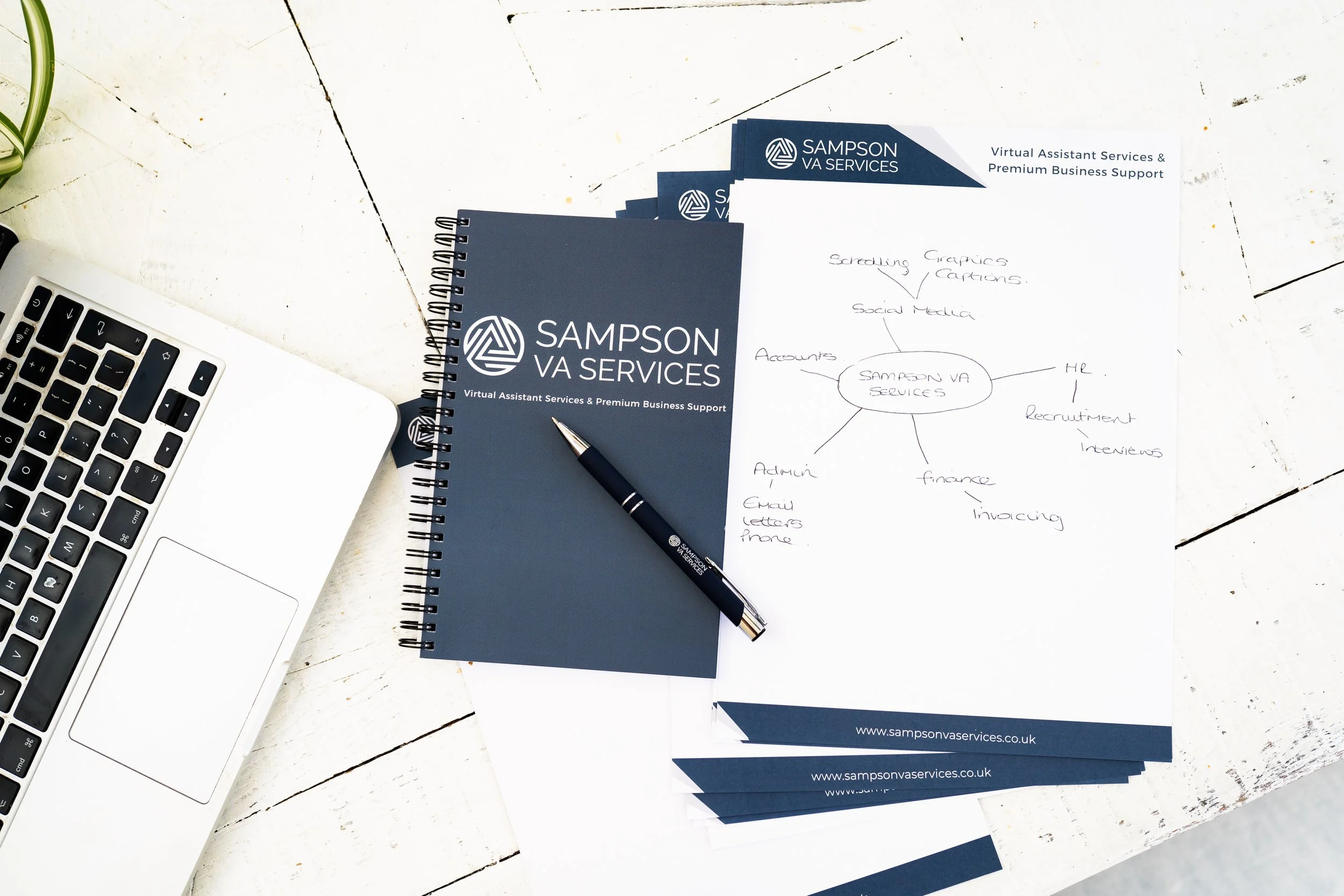 Branded Sampson VA Services notebook and documents on a desk beside a laptop, with handwritten notes outlining business support services.