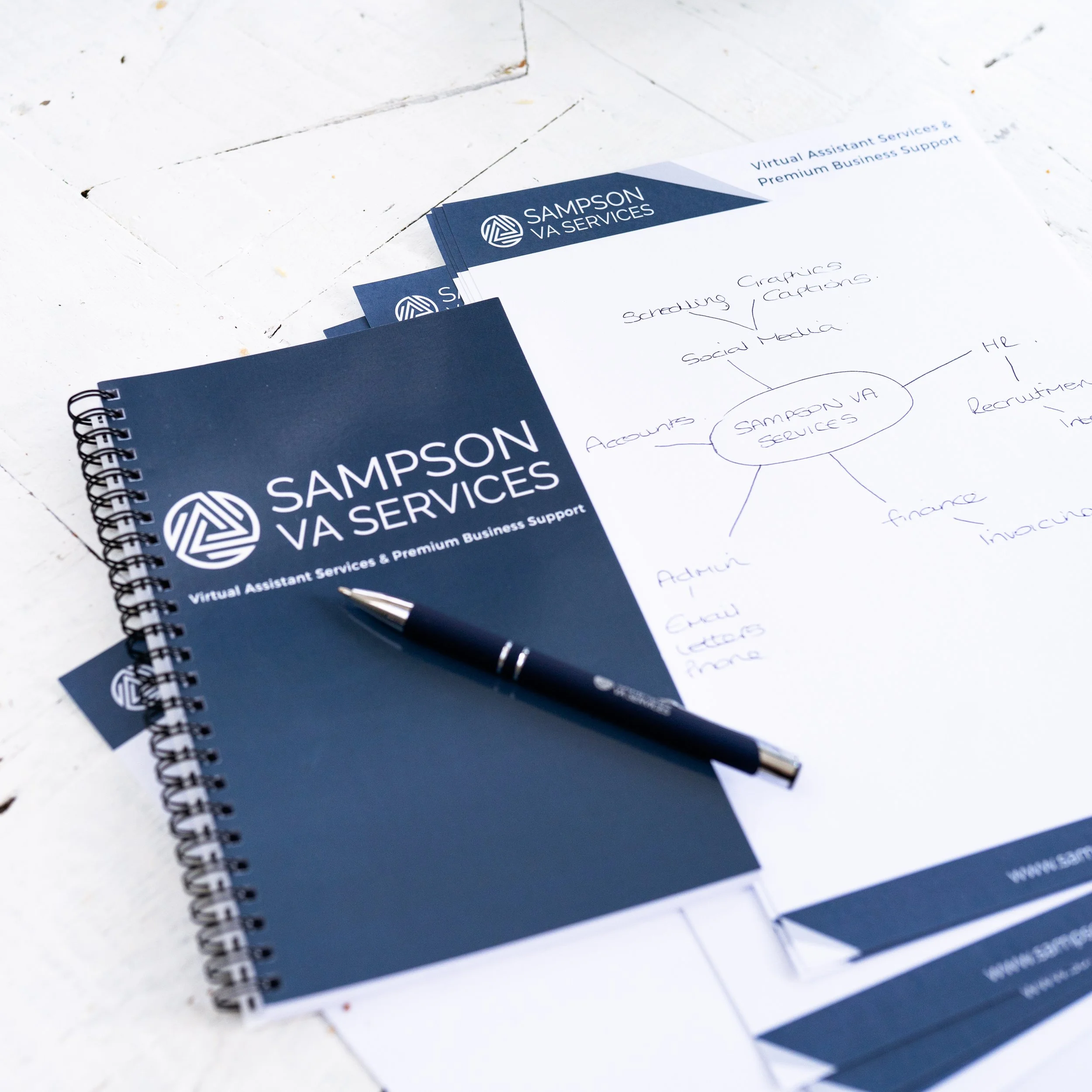 Close-up of Sampson VA Services branded stationery, including a notebook and printed materials with handwritten notes outlining services such as admin, HR, finance and social media.