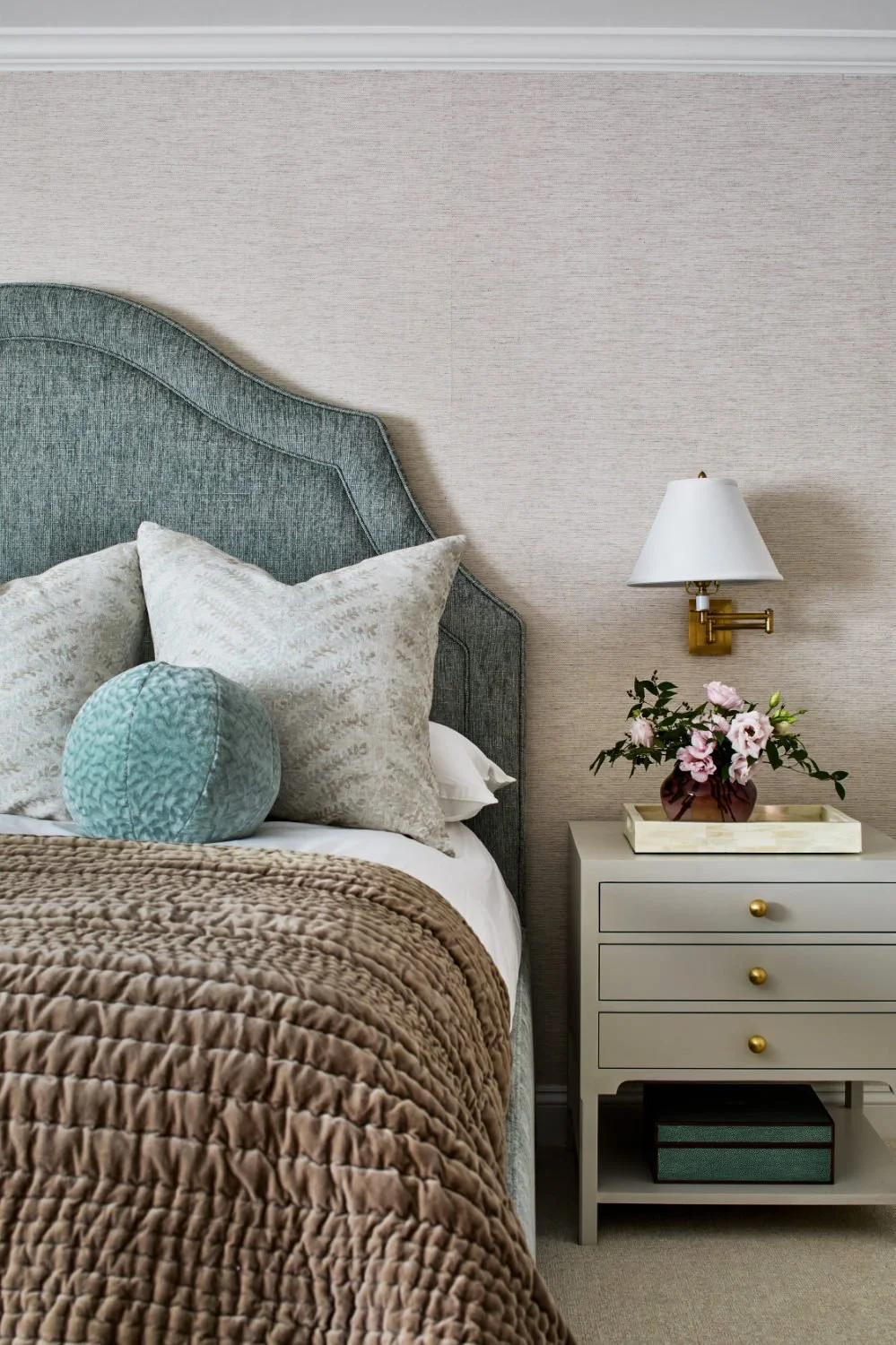 A bedroom with a bed featuring multiple pillows, a headboard, and a nightstand with a potted plant and a lamp.