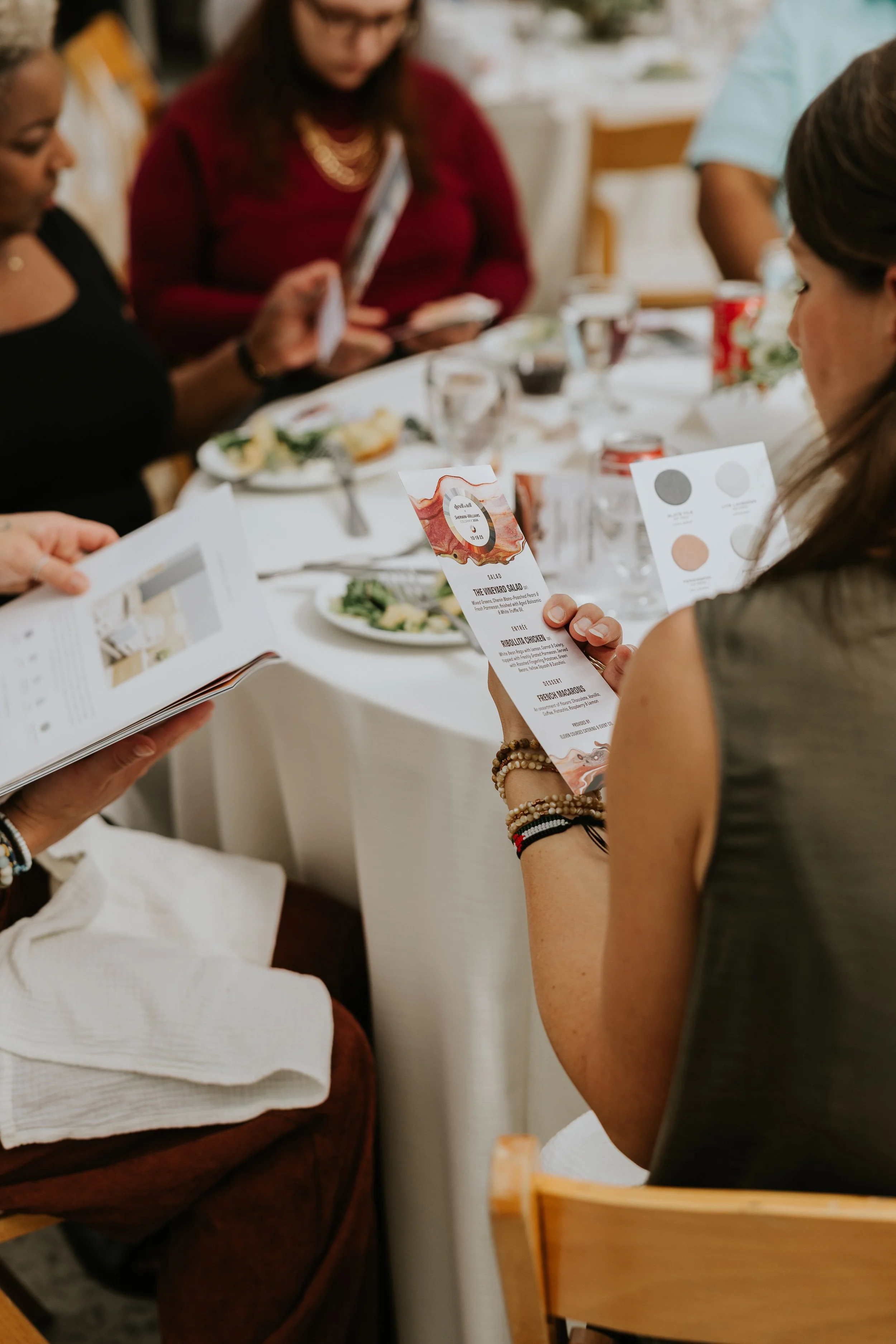 People sitting at a dining table reading menus, with plates of food and drinks, during a meal or gathering.