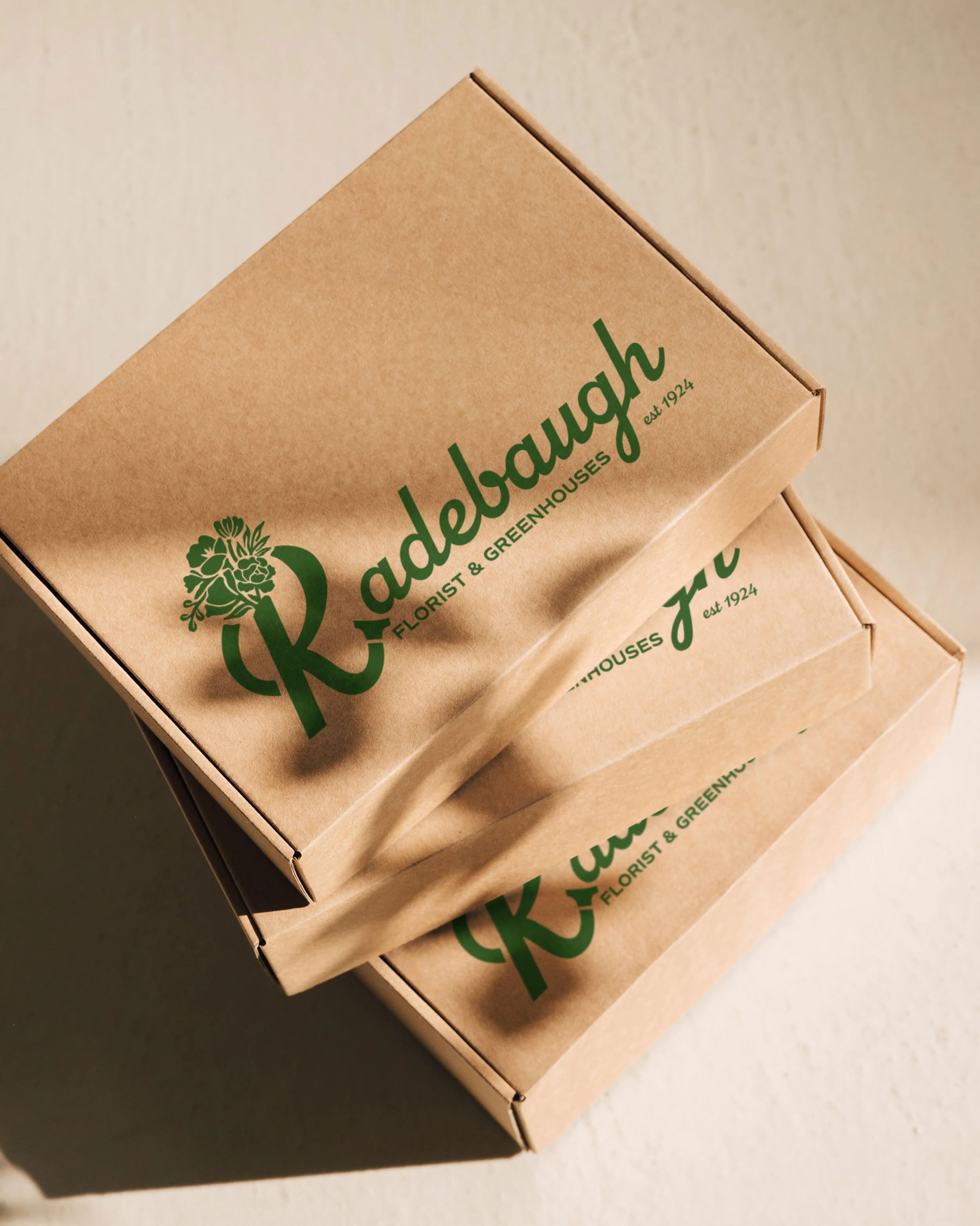 Three cardboard boxes with green lettering and logo for Radebaugh Florist & Greenhouses, stacked together, on a light-colored surface.