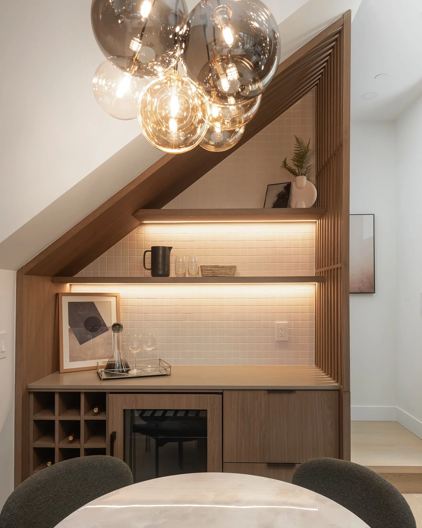 Warm light, layered textures ✨

A statement cluster pendant sets the mood with a soft, ambient glow, while integrated shelf lighting adds depth and function&mdash;highlighting every detail without stealing the spotlight. Rich wood millwork brings war