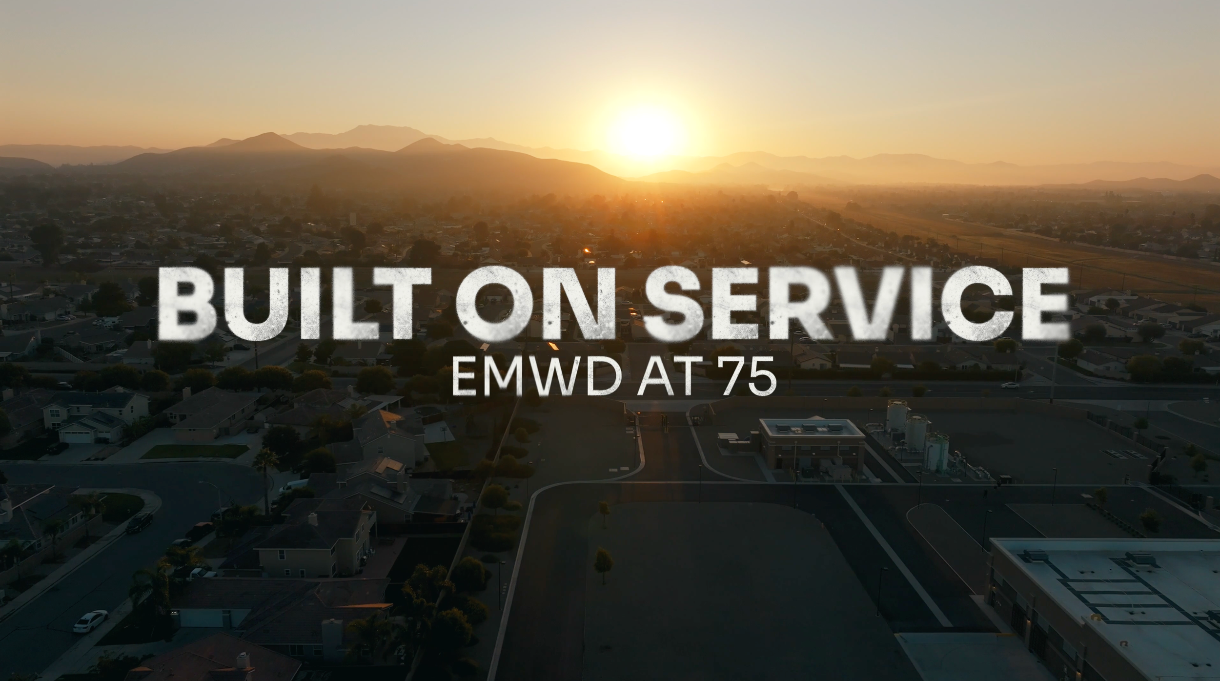 Sunset over a suburban neighborhood with hills in the background and text overlay reading 'Built on Service, EMWD at 75'.