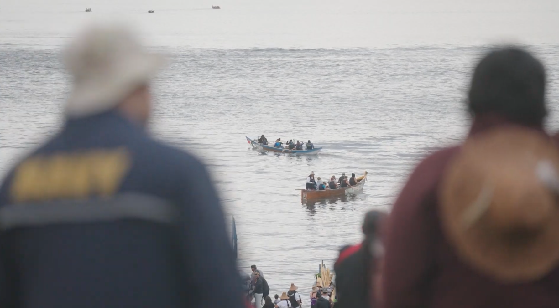A group of diverse young people paddling in a traditional wooden canoe on open water during daytime.