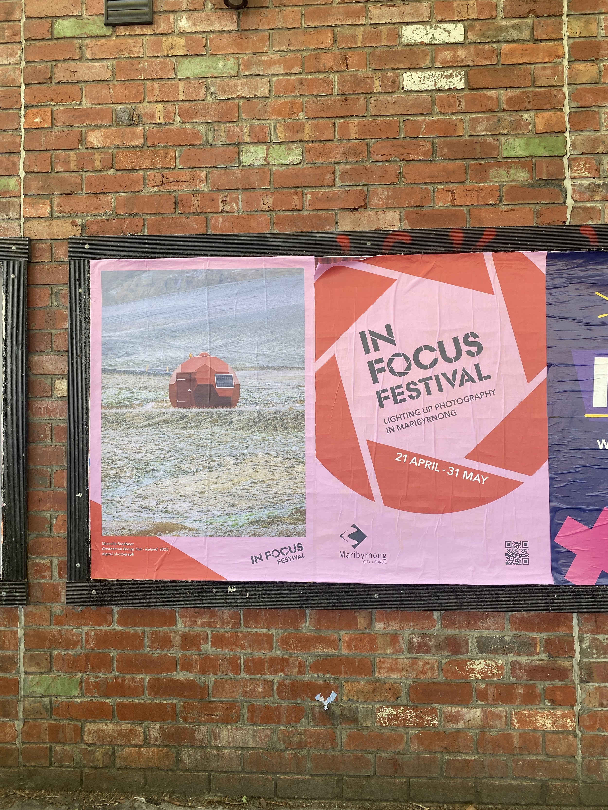 A brick wall with a partially visible poster that shows a geodesic dome on water and text indicating an event called 'IN FOCUS FESTIVAL' in Maribyrnong, including the dates '21 April - 31 May'.