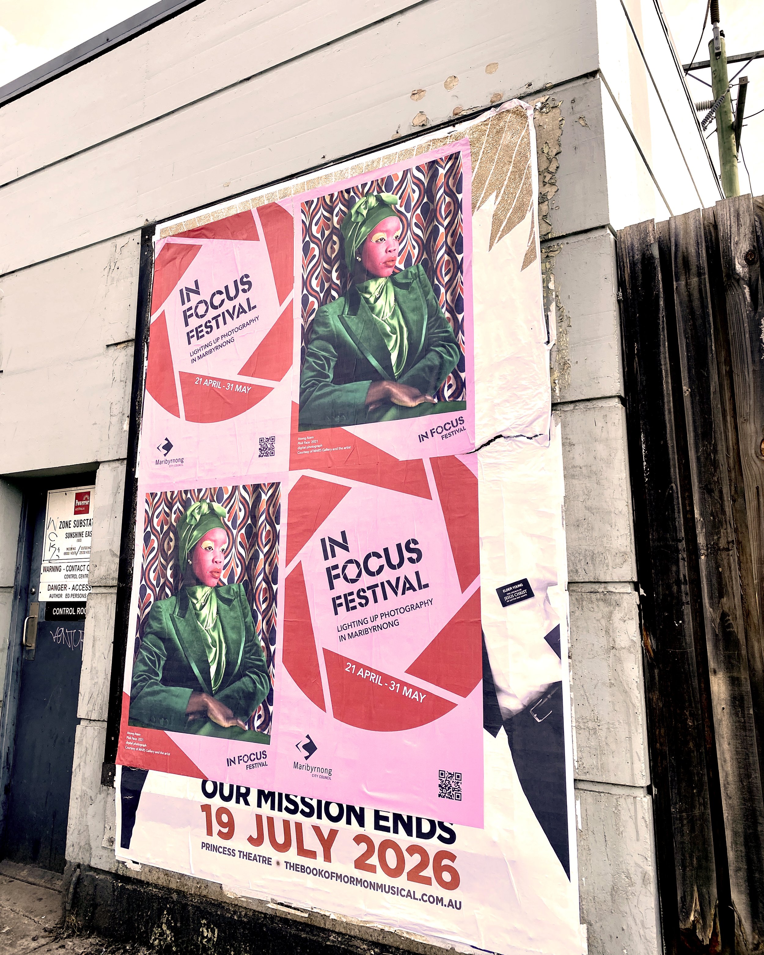 A large poster advertising the In Focus Festival on a concrete wall. The poster features a woman in a vibrant green suit and headscarf with makeup, against a patterned background. The festival runs from April 21 to May 31, 2026, in Maribyrnong, Australia, and the website is listed at the bottom.