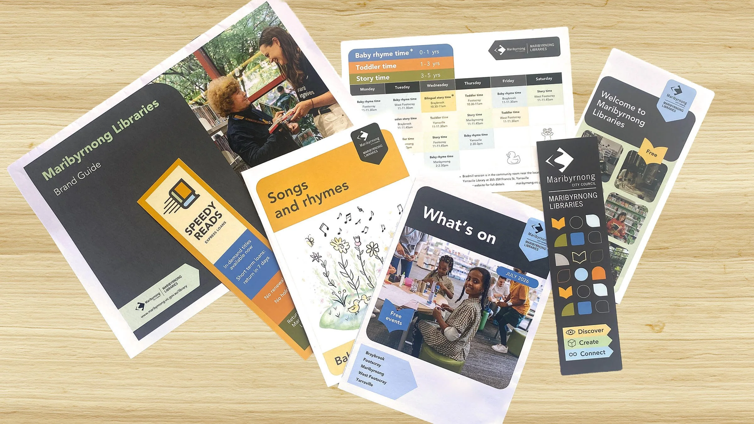Brochures and flyers for Maribyrnong Libraries on a wooden surface, promoting programs, books, and events for children and adults.